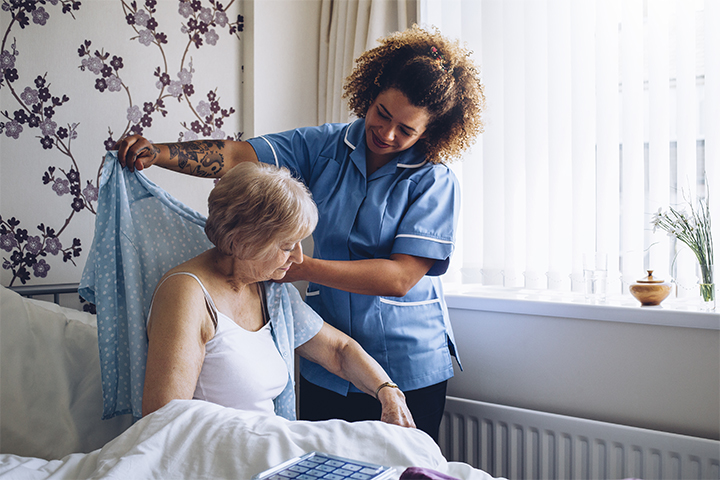 A nurse is helping an older woman in bed.