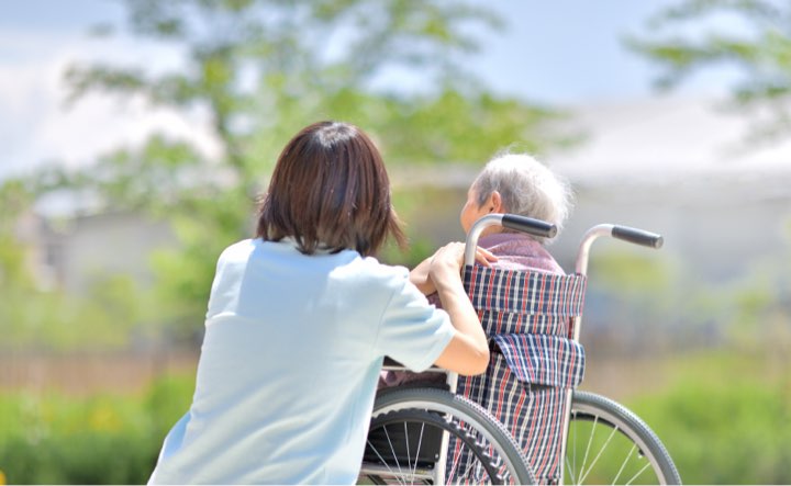 A woman is helping an old man ride his bike.