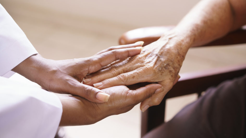 A person holding an elderly hand over another persons arm.